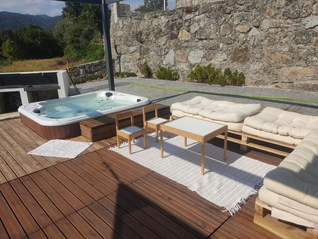 Jacuzzi sur la terrasse en bois, avec des canapés en palettes et le barbecue adossé au mur de pierre