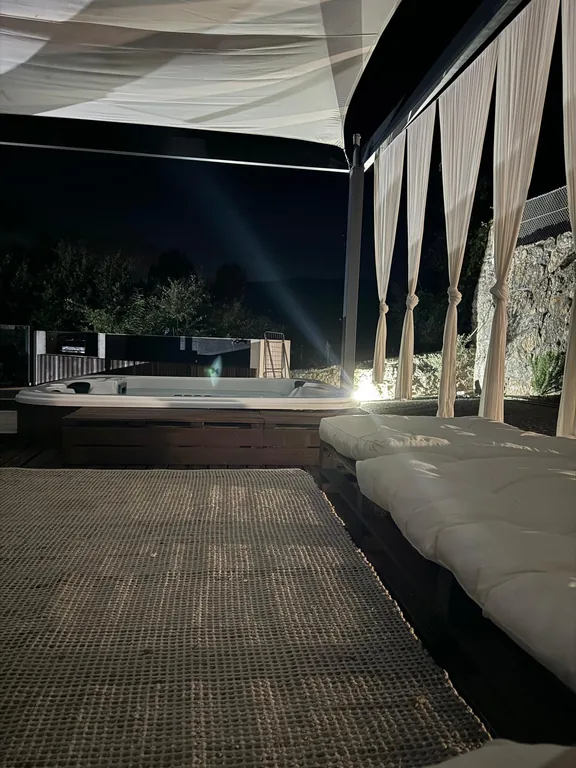 Le jacuzzi à la tombée de la nuit, sous la voile d'ombrage, les rideaux et le matelas de la terrasse éclairés